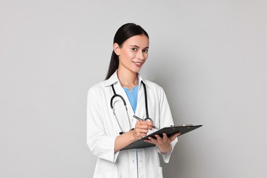 Photo of Smiling nurse with clipboard writing notes on grey background