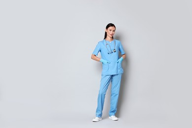 Photo of Beautiful nurse in uniform on grey background. Space for text