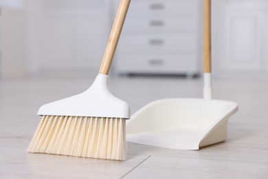 Photo of Cleaning broom and dustpan on wooden floor indoors