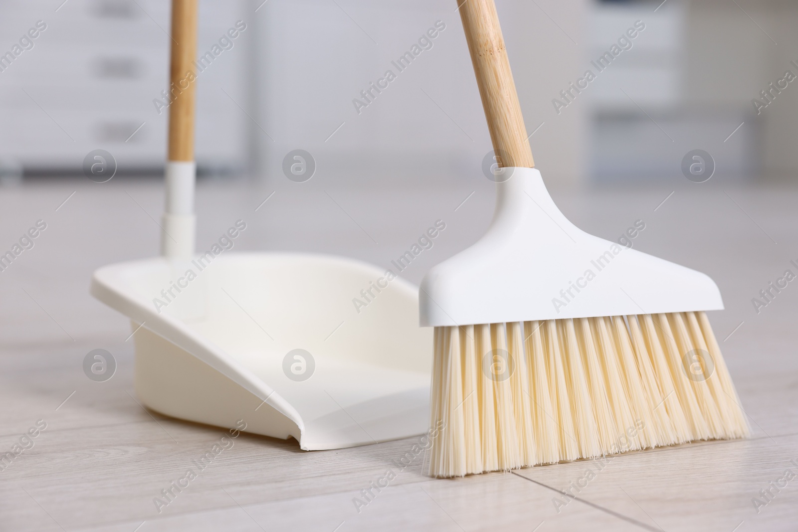 Photo of Cleaning broom and dustpan on wooden floor indoors