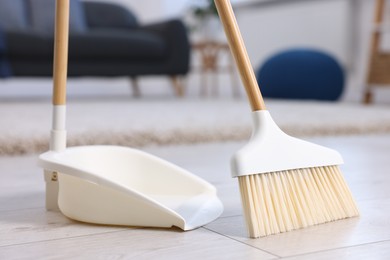 Photo of Cleaning broom and dustpan on wooden floor indoors