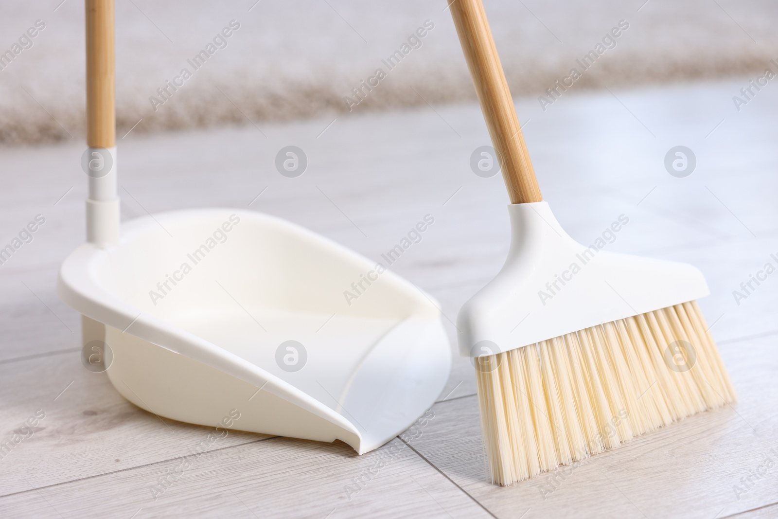 Photo of Cleaning broom and dustpan on wooden floor indoors