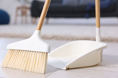 Photo of Cleaning broom and dustpan on wooden floor indoors