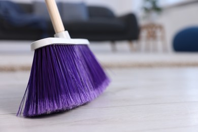 Cleaning broom on wooden floor indoors, closeup. Space for text