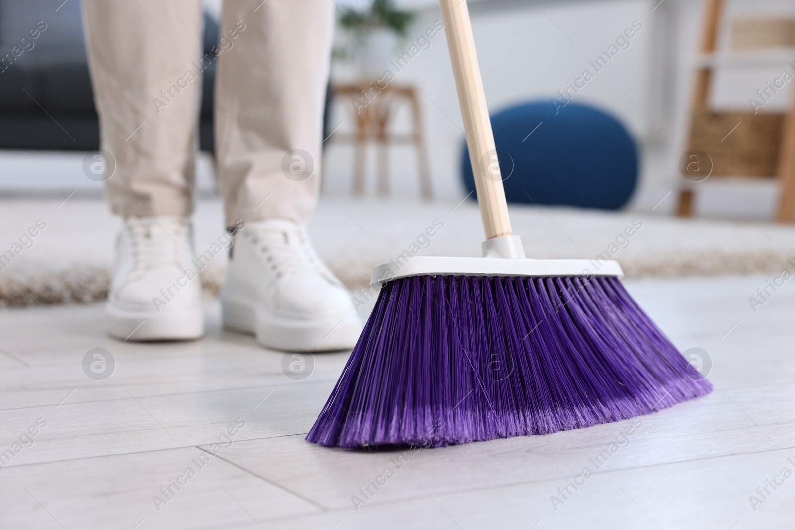 Photo of Woman with broom sweeping floor indoors, closeup