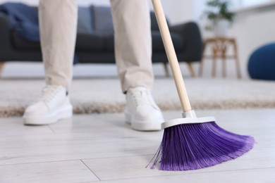 Photo of Woman with broom sweeping floor indoors, closeup