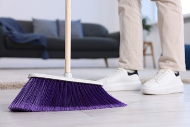 Photo of Woman with broom sweeping floor indoors, closeup