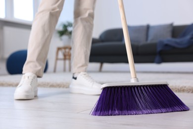 Photo of Woman with broom sweeping floor indoors, closeup