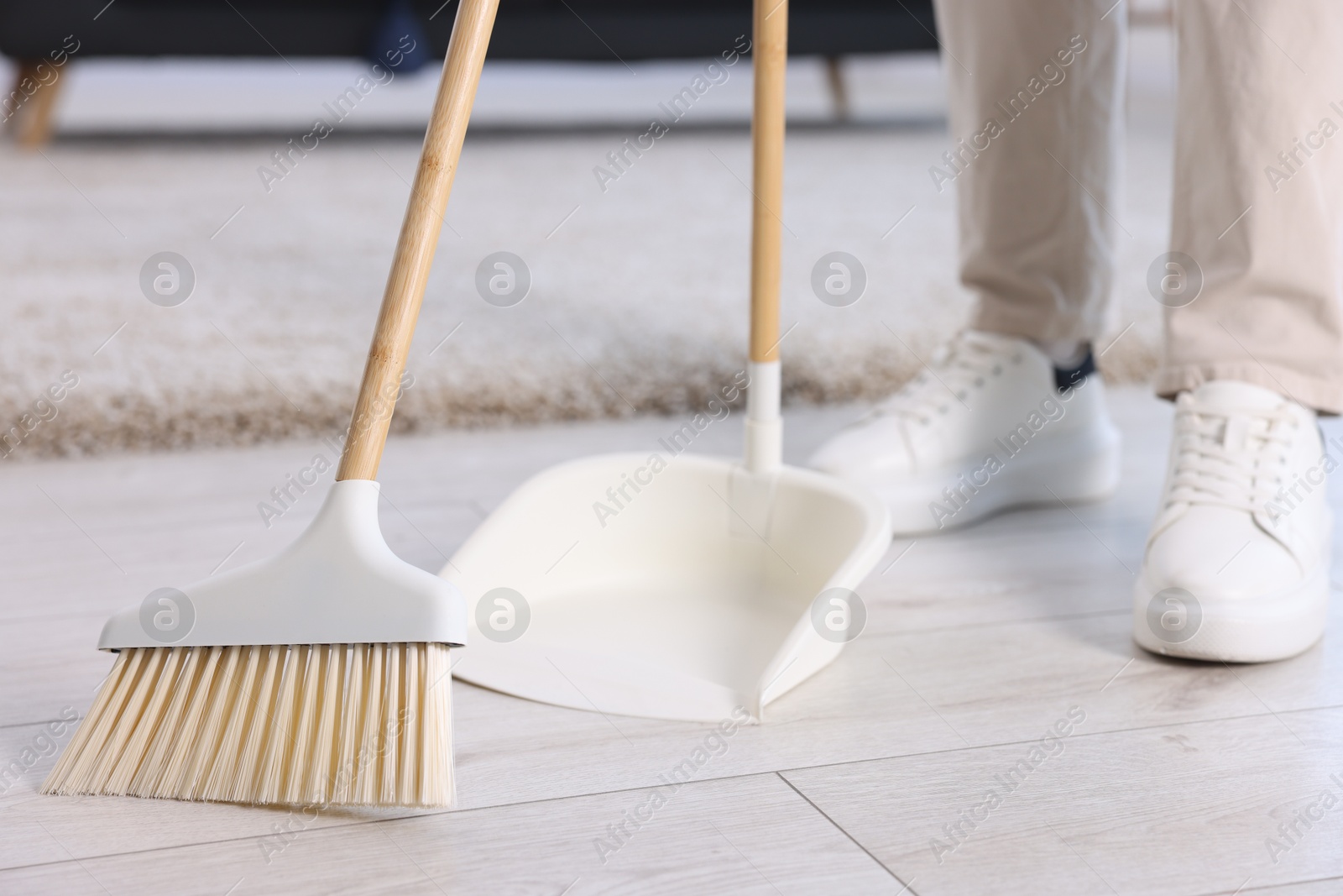 Photo of Woman with broom and dustpan cleaning floor indoors, closeup