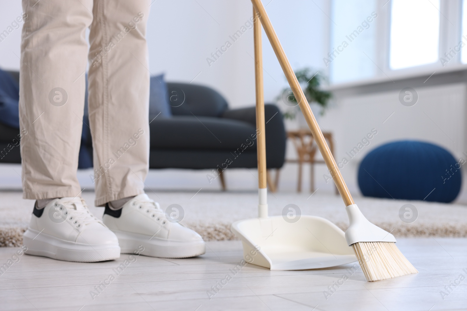 Photo of Woman with broom and dustpan cleaning floor indoors, closeup