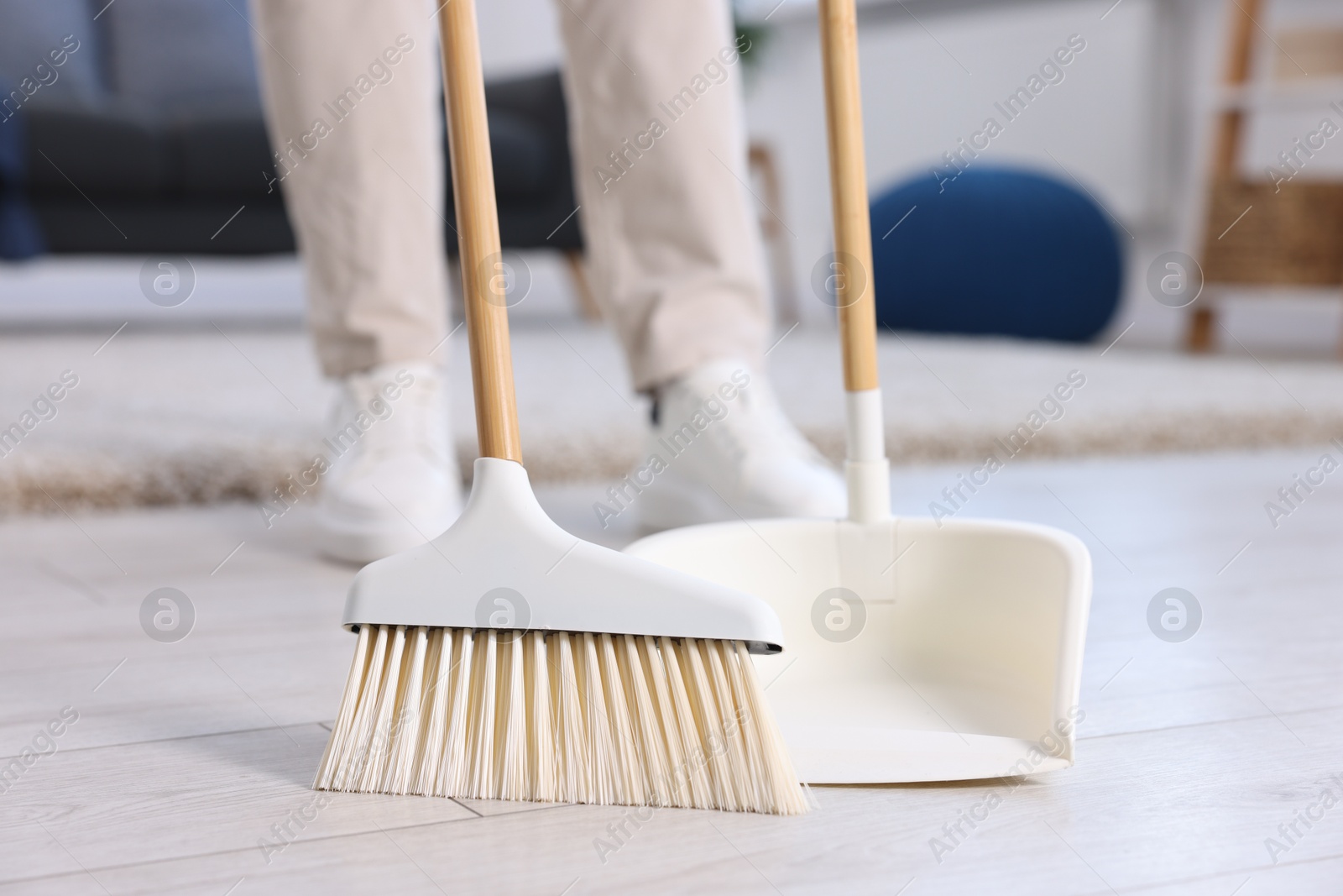 Photo of Woman with broom and dustpan cleaning floor indoors, closeup