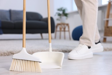 Photo of Woman with broom and dustpan cleaning floor indoors, closeup