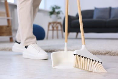 Woman with broom and dustpan cleaning floor indoors, closeup