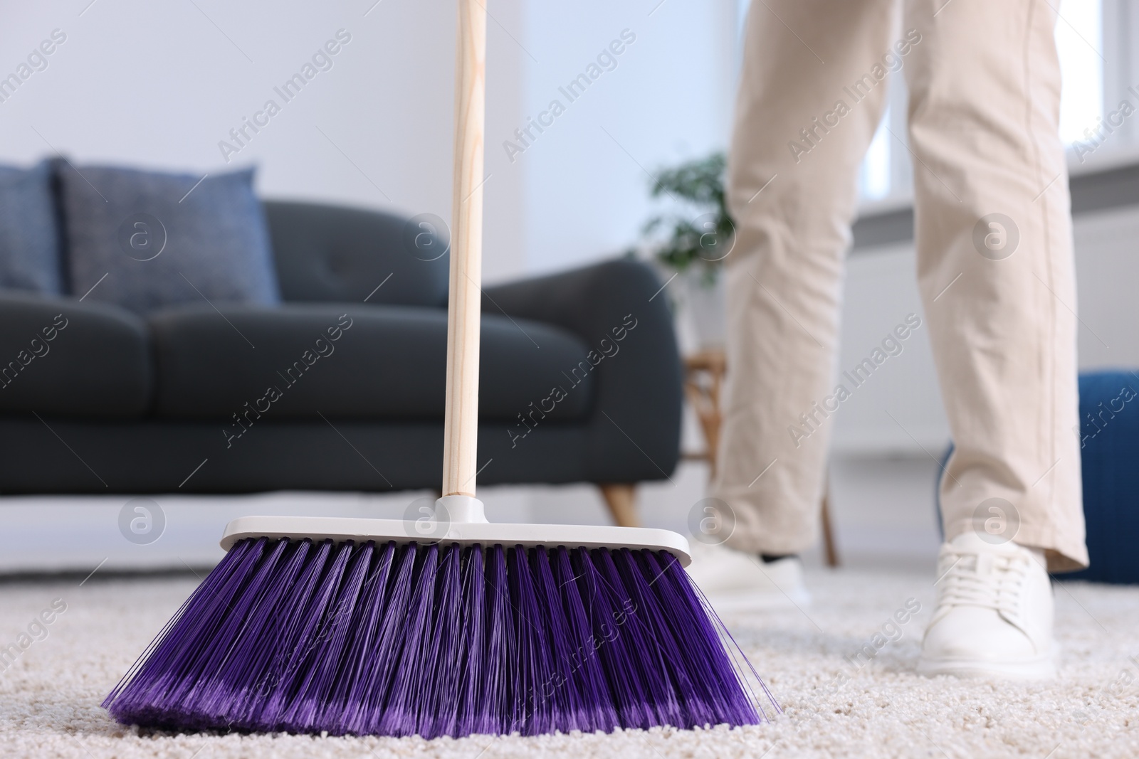 Photo of Woman with broom sweeping carpet indoors, closeup