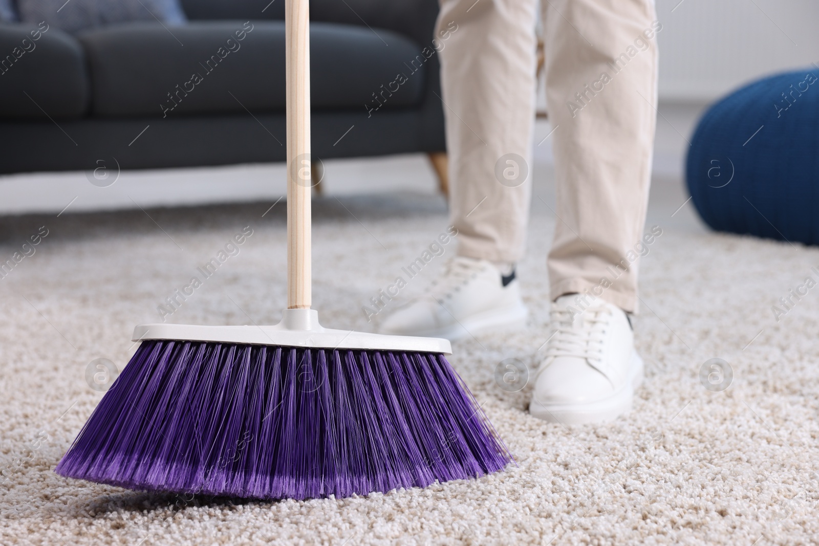 Photo of Woman with broom sweeping carpet indoors, closeup