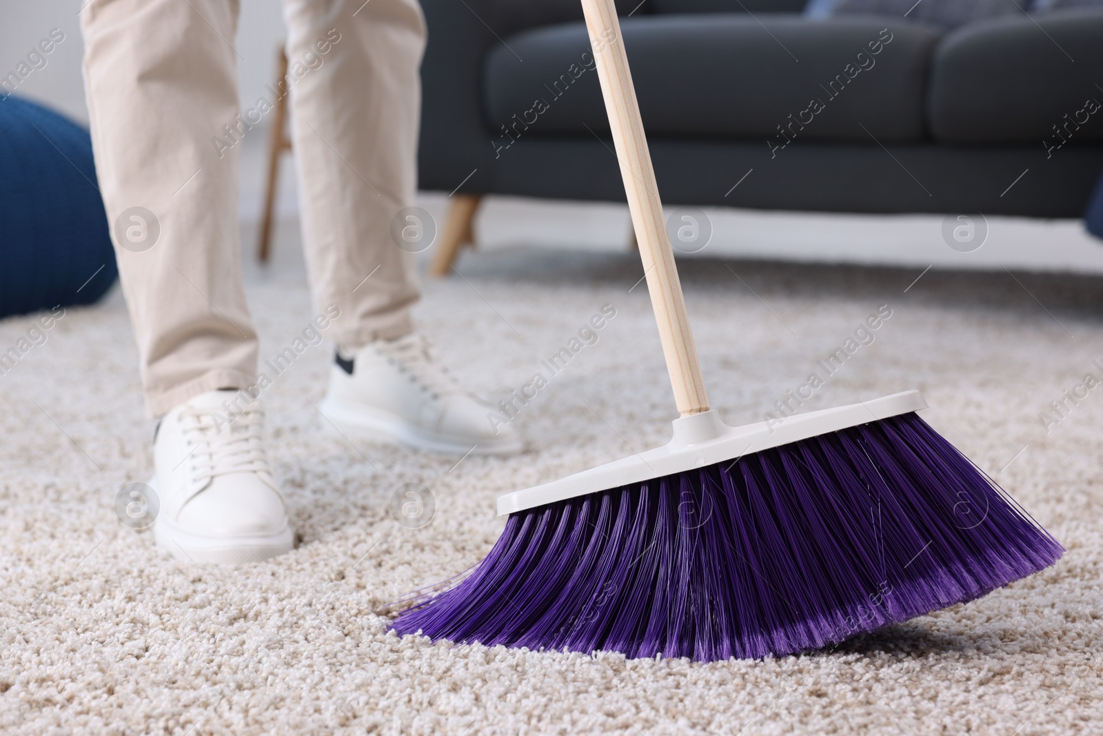 Photo of Woman with broom sweeping carpet indoors, closeup