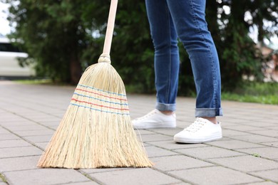 Photo of Woman with corn straw broom sweeping pavement outdoors, closeup