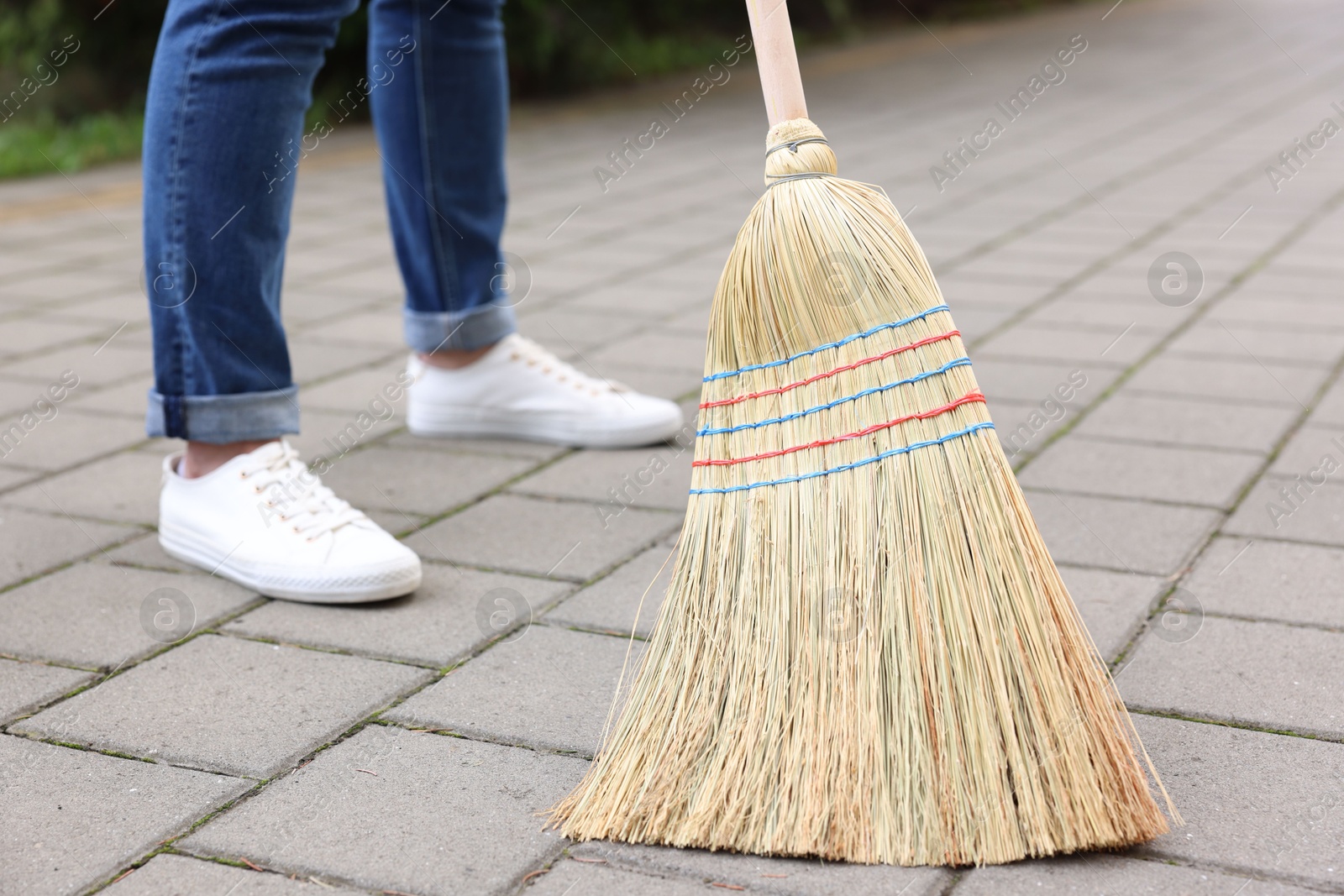 Photo of Woman with corn straw broom sweeping pavement outdoors, closeup