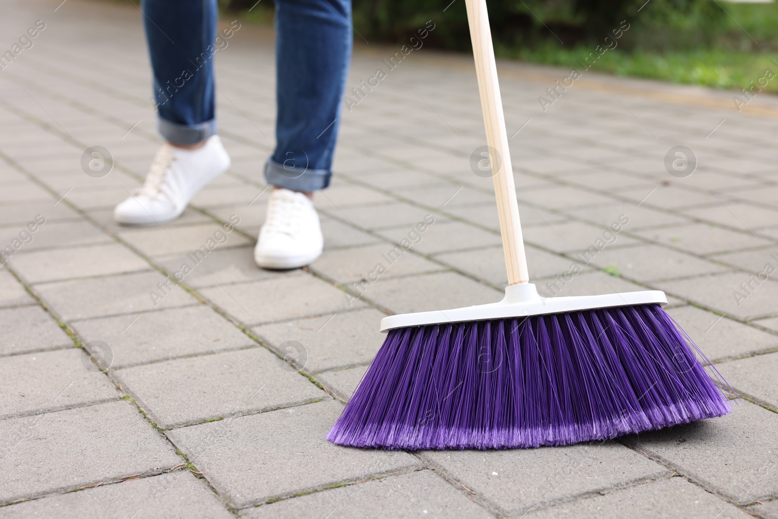 Photo of Woman with broom sweeping pavement outdoors, closeup