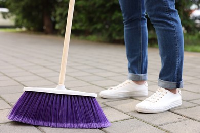 Woman with broom sweeping pavement outdoors, closeup