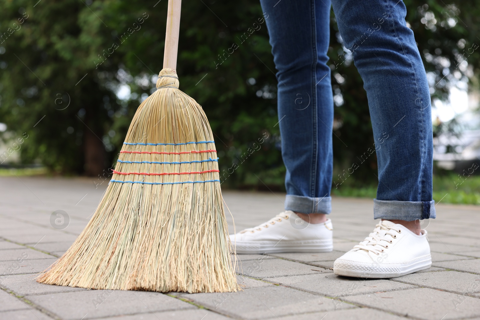 Photo of Woman with corn straw broom sweeping pavement outdoors, closeup