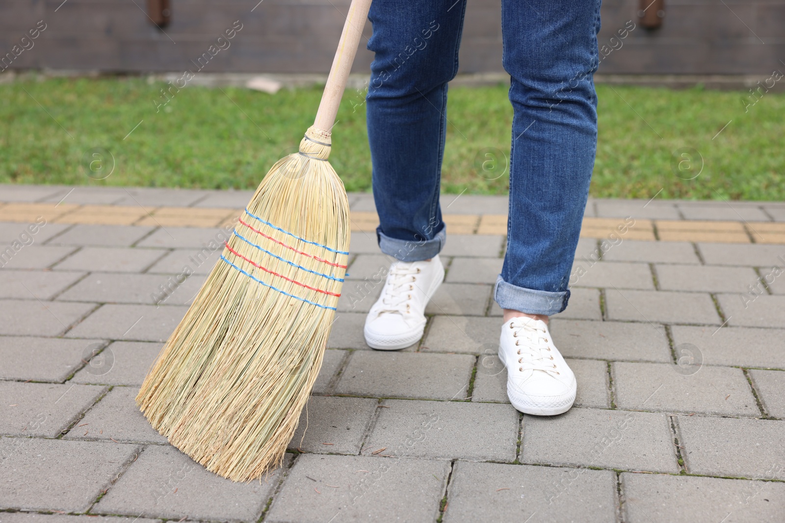 Photo of Woman with corn straw broom sweeping pavement outdoors, closeup