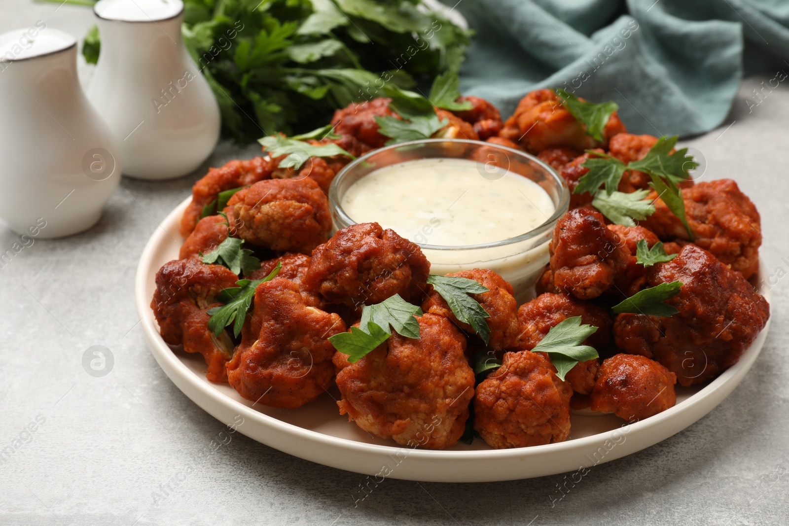 Photo of Baked cauliflower buffalo wings with parsley and sauce on light grey table, closeup