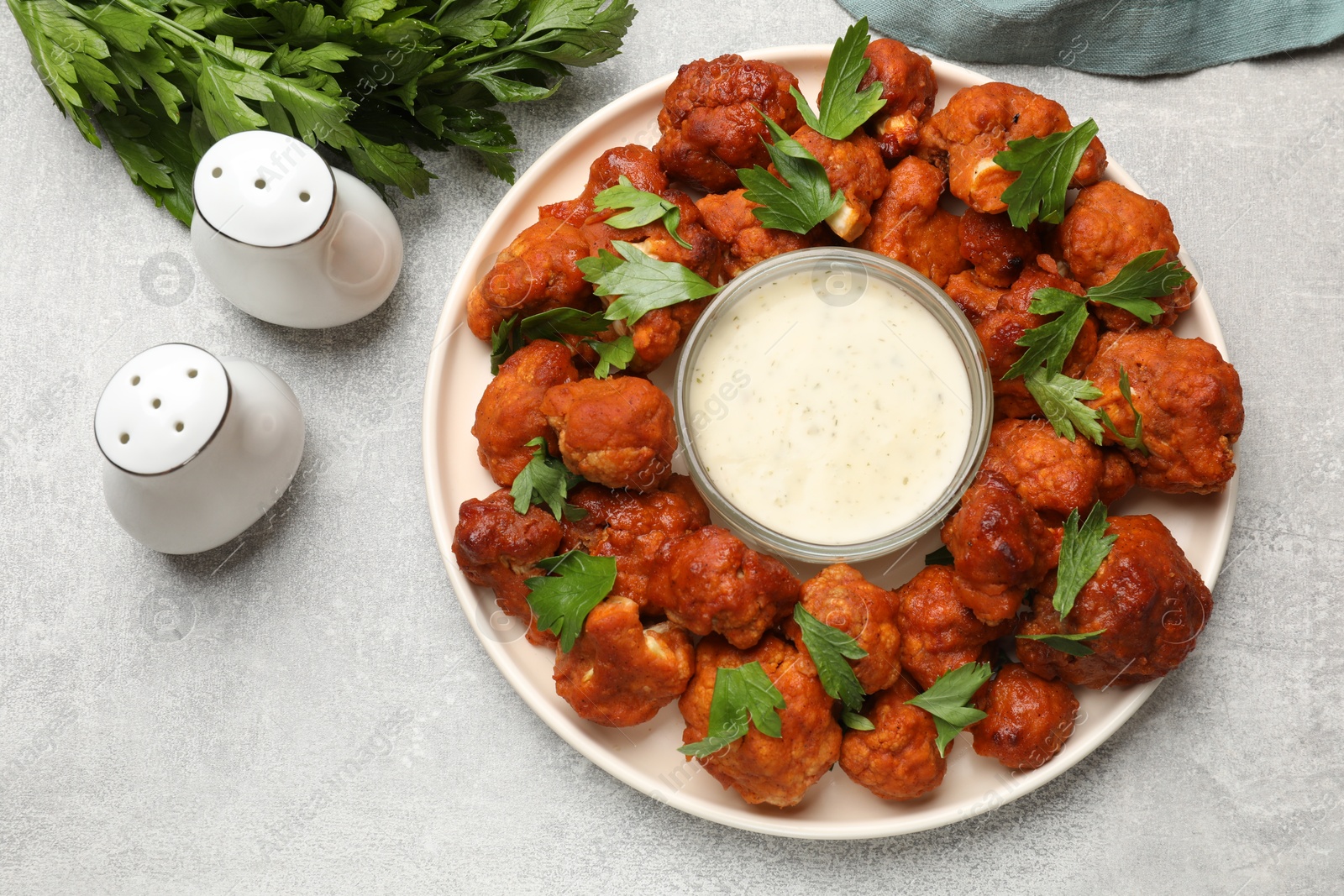 Photo of Baked cauliflower buffalo wings with parsley and sauce on light grey table, top view