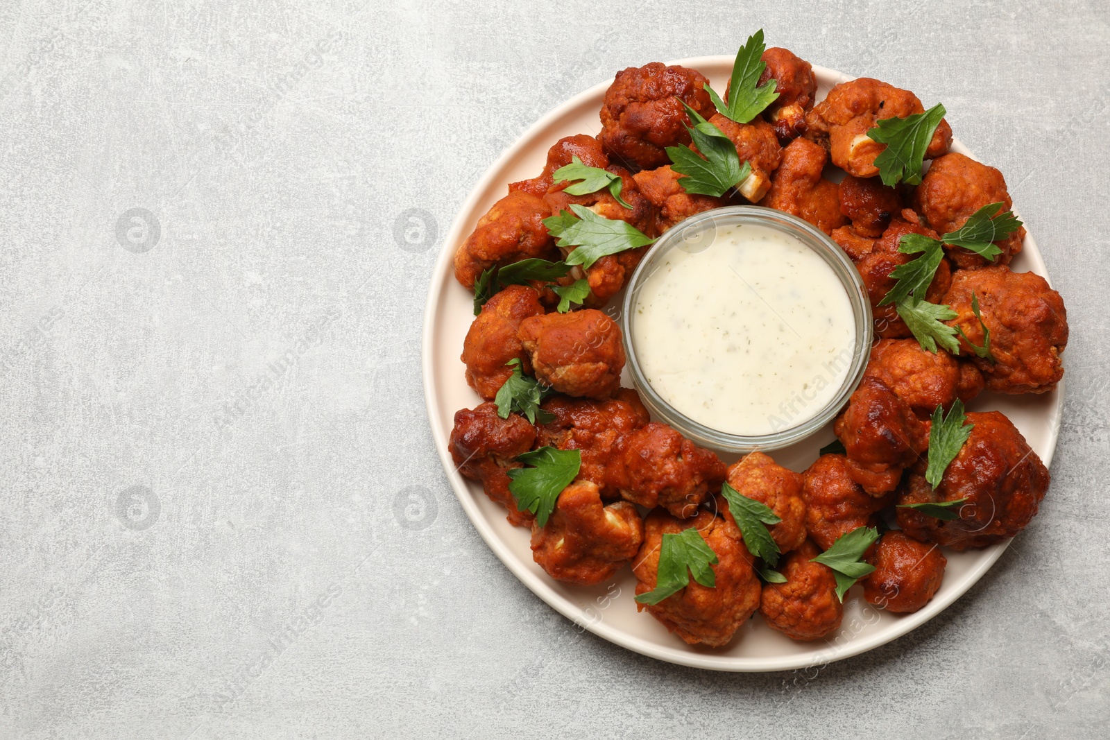 Photo of Baked cauliflower buffalo wings with parsley and sauce on light grey table, top view. Space for text