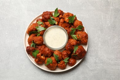 Photo of Baked cauliflower buffalo wings with parsley and sauce on light grey table, top view