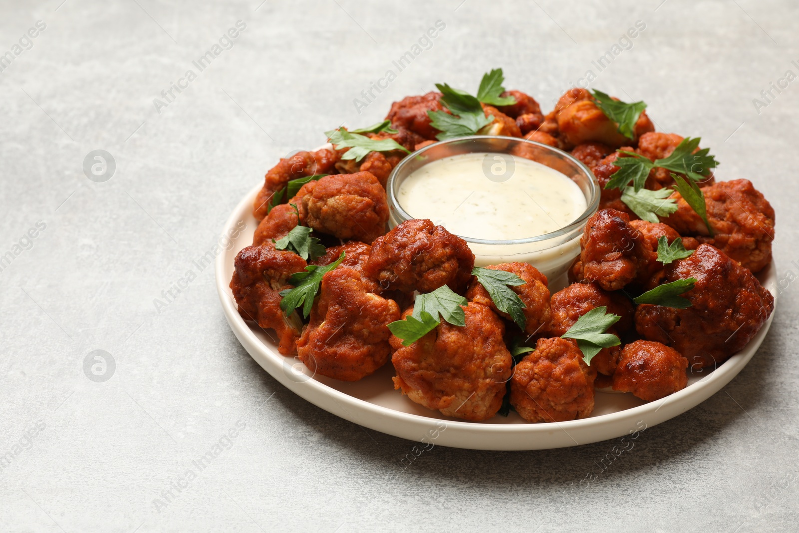 Photo of Baked cauliflower buffalo wings with parsley and sauce on light grey table