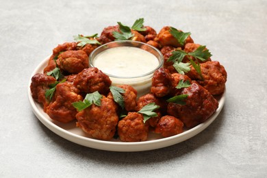 Photo of Baked cauliflower buffalo wings with parsley and sauce on light grey table, closeup