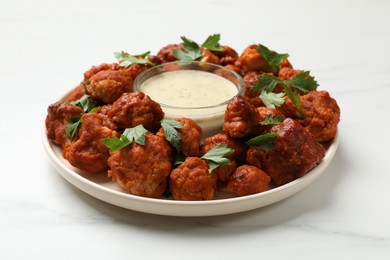 Photo of Baked cauliflower buffalo wings with parsley and sauce on white marble table, closeup