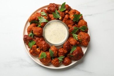 Photo of Baked cauliflower buffalo wings with parsley and sauce on white marble table, top view