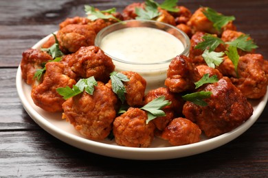 Photo of Baked cauliflower buffalo wings with parsley and sauce on wooden table, closeup