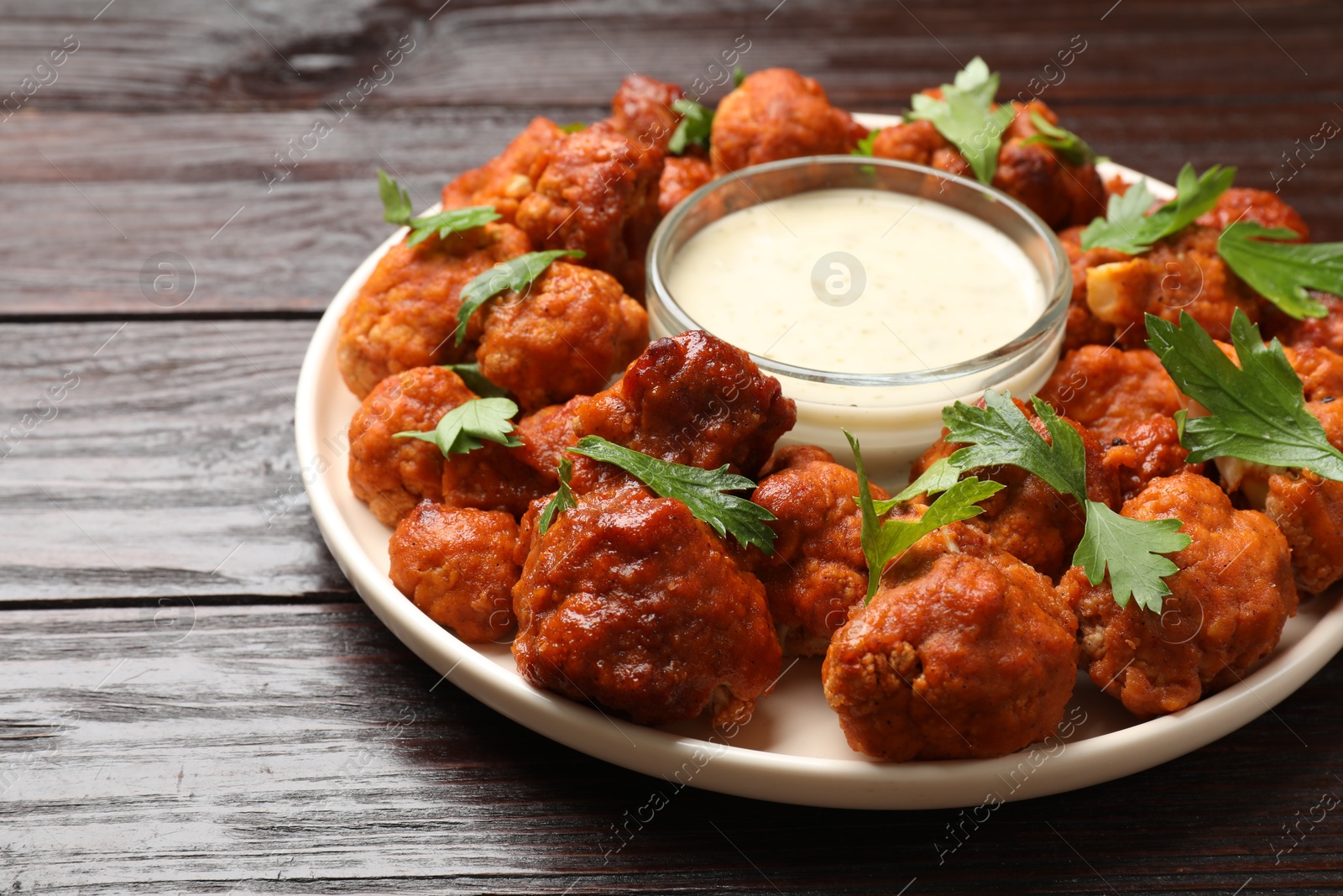 Photo of Baked cauliflower buffalo wings with parsley and sauce on wooden table, closeup