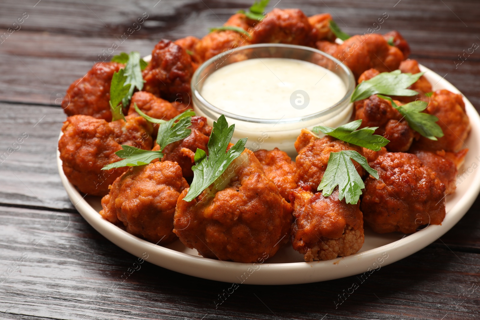 Photo of Baked cauliflower buffalo wings with parsley and sauce on wooden table, closeup