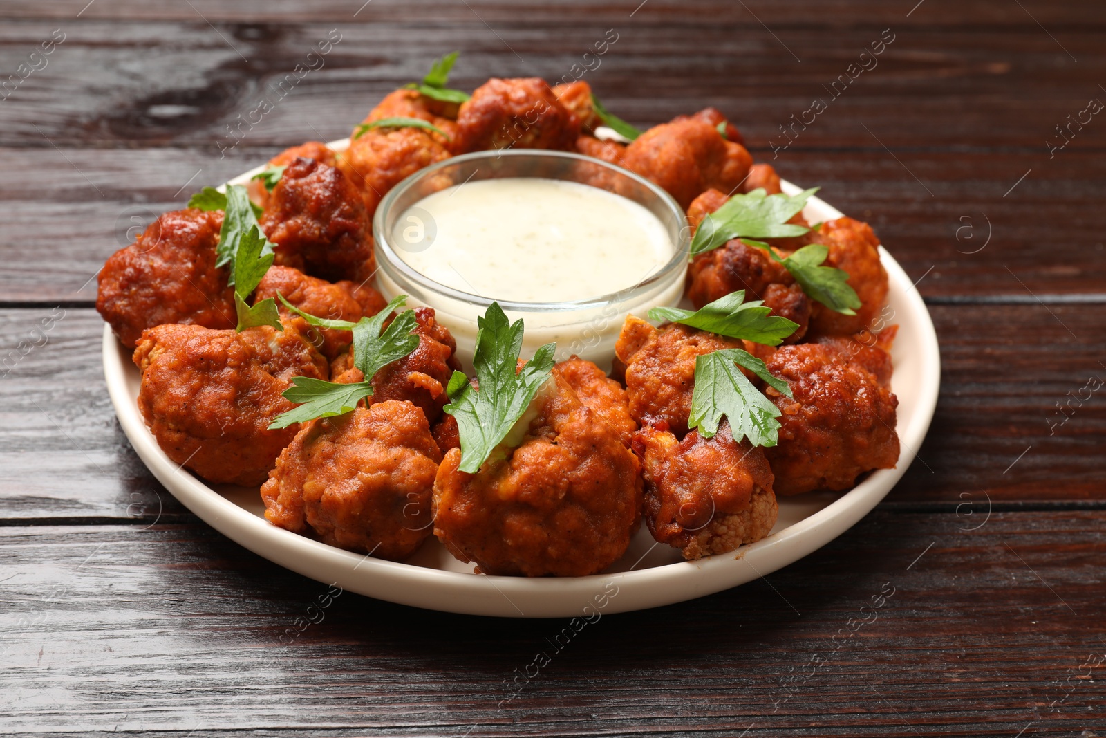 Photo of Baked cauliflower buffalo wings with parsley and sauce on wooden table, closeup