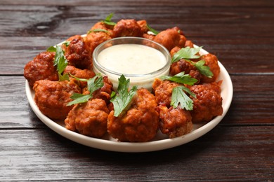 Photo of Baked cauliflower buffalo wings with parsley and sauce on wooden table, closeup