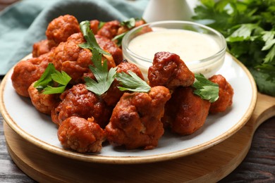 Photo of Baked cauliflower buffalo wings, parsley and sauce on wooden table, closeup