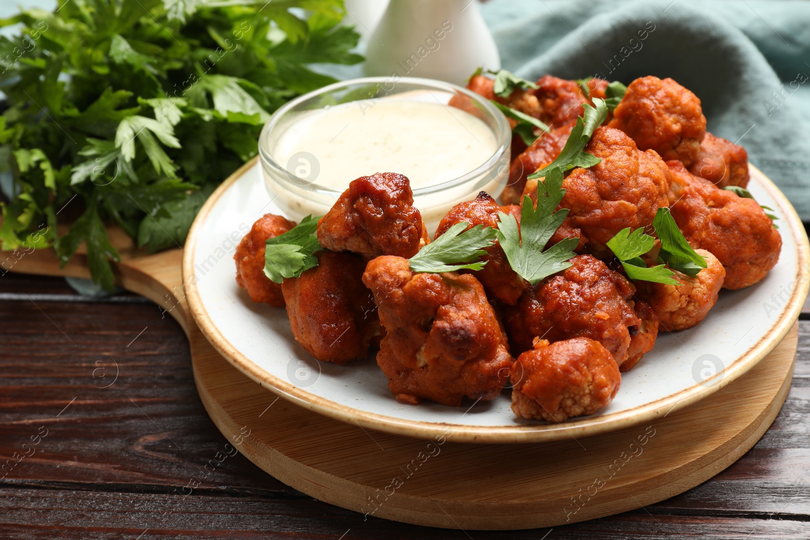 Photo of Baked cauliflower buffalo wings, parsley and sauce on wooden table, closeup