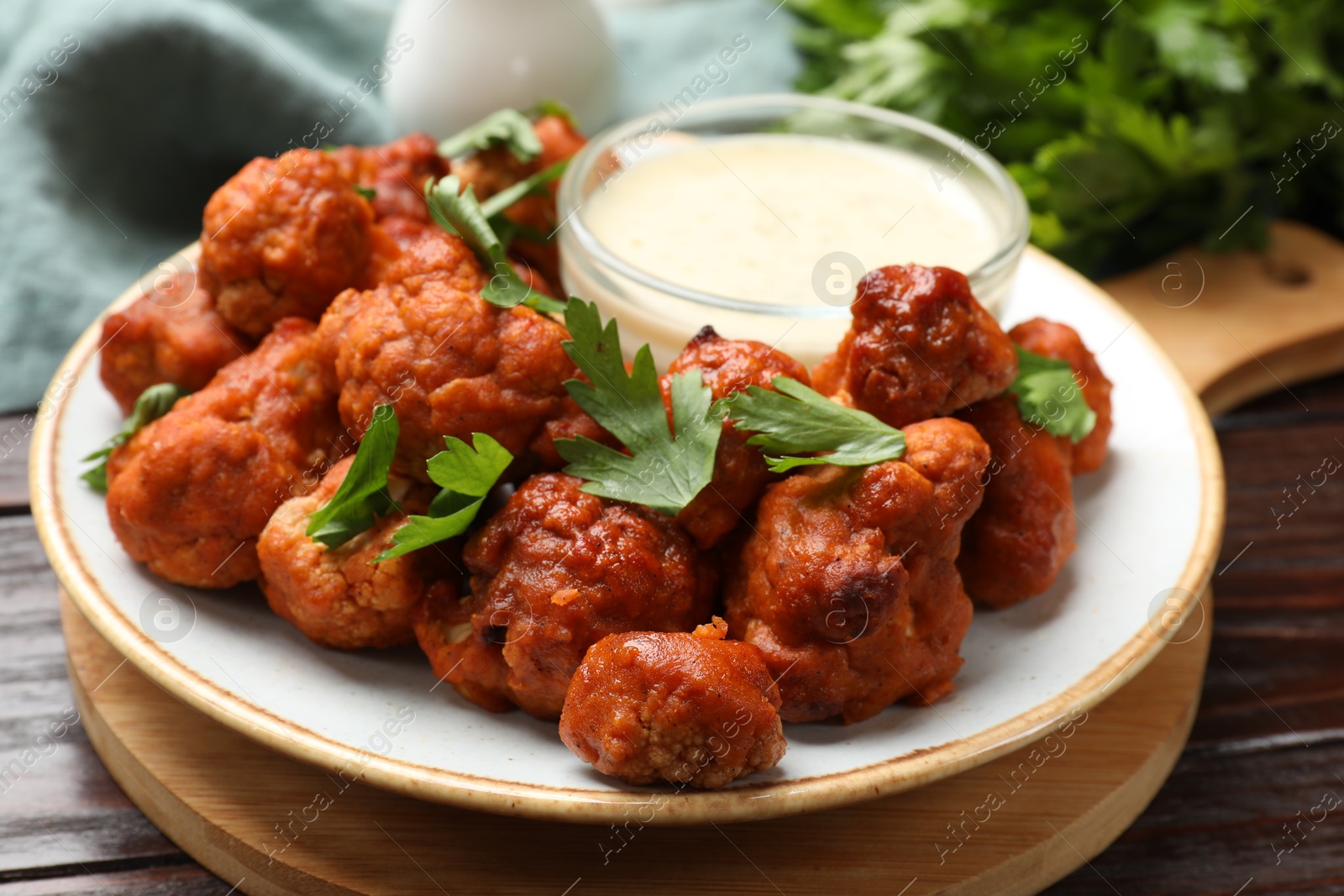 Photo of Baked cauliflower buffalo wings, parsley and sauce on wooden table, closeup