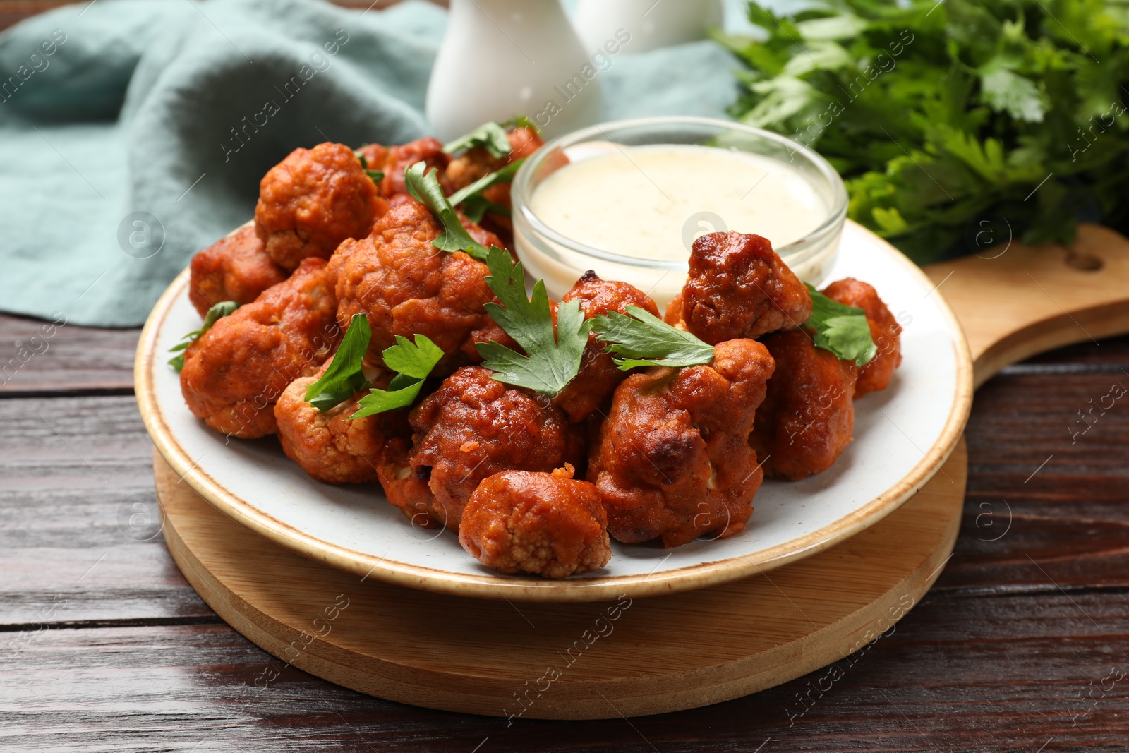 Photo of Baked cauliflower buffalo wings, parsley and sauce on wooden table, closeup