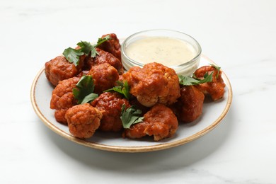 Photo of Baked cauliflower buffalo wings with parsley and sauce on white marble table