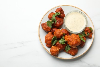 Photo of Baked cauliflower buffalo wings with parsley and sauce on white marble table, top view. Space for text