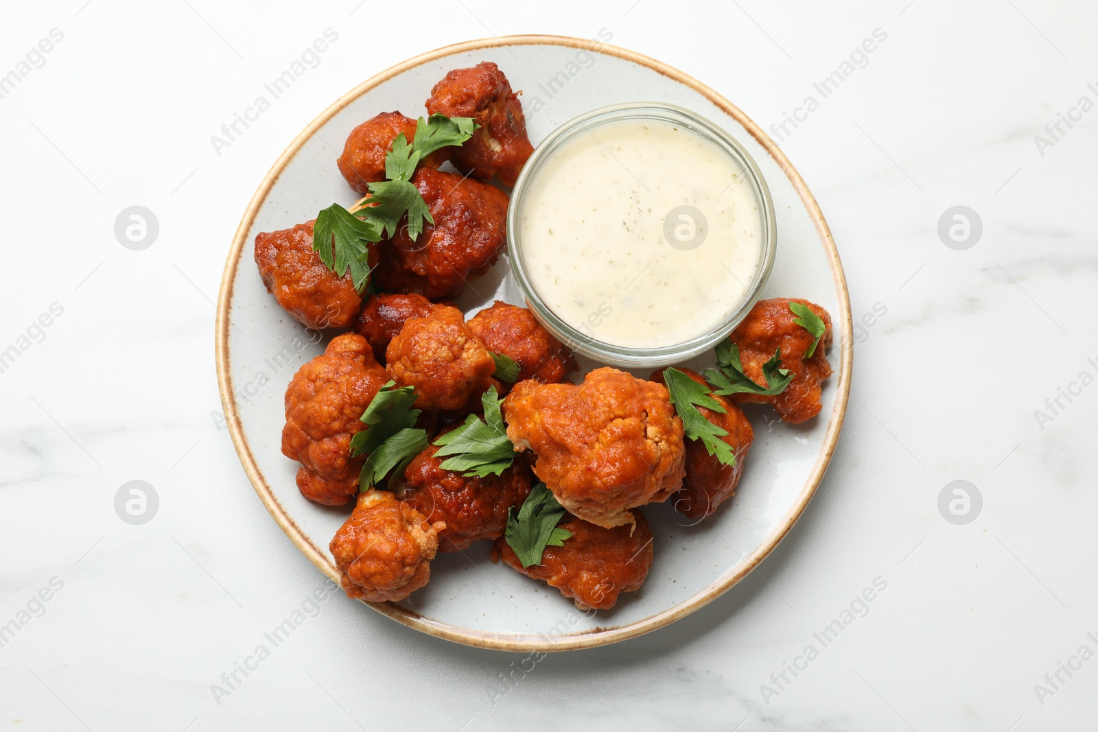 Photo of Baked cauliflower buffalo wings with parsley and sauce on white marble table, top view