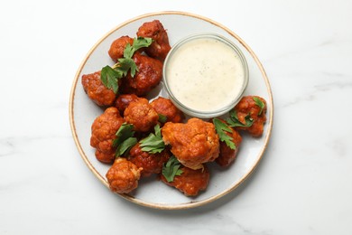 Photo of Baked cauliflower buffalo wings with parsley and sauce on white marble table, top view