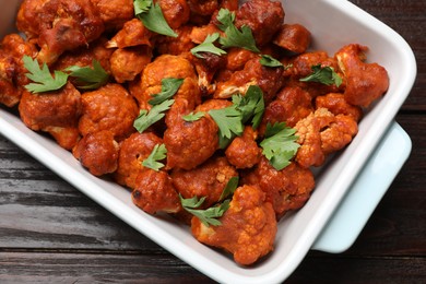 Photo of Baked cauliflower buffalo wings with parsley in baking dish on wooden table, top view