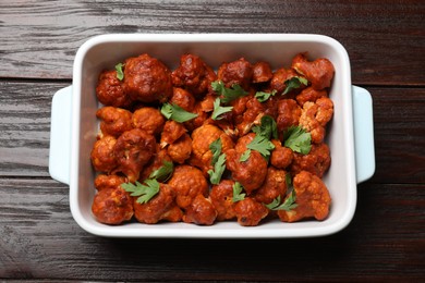 Photo of Baked cauliflower buffalo wings with parsley in baking dish on wooden table, top view