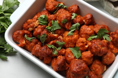 Photo of Baked cauliflower buffalo wings in baking dish and parsley on white table, top view